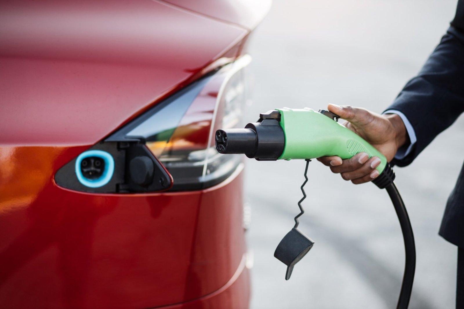 Gros plan de la main mâle tenant une bougie de charge électrique verte pour la voiture rouge de luxe.