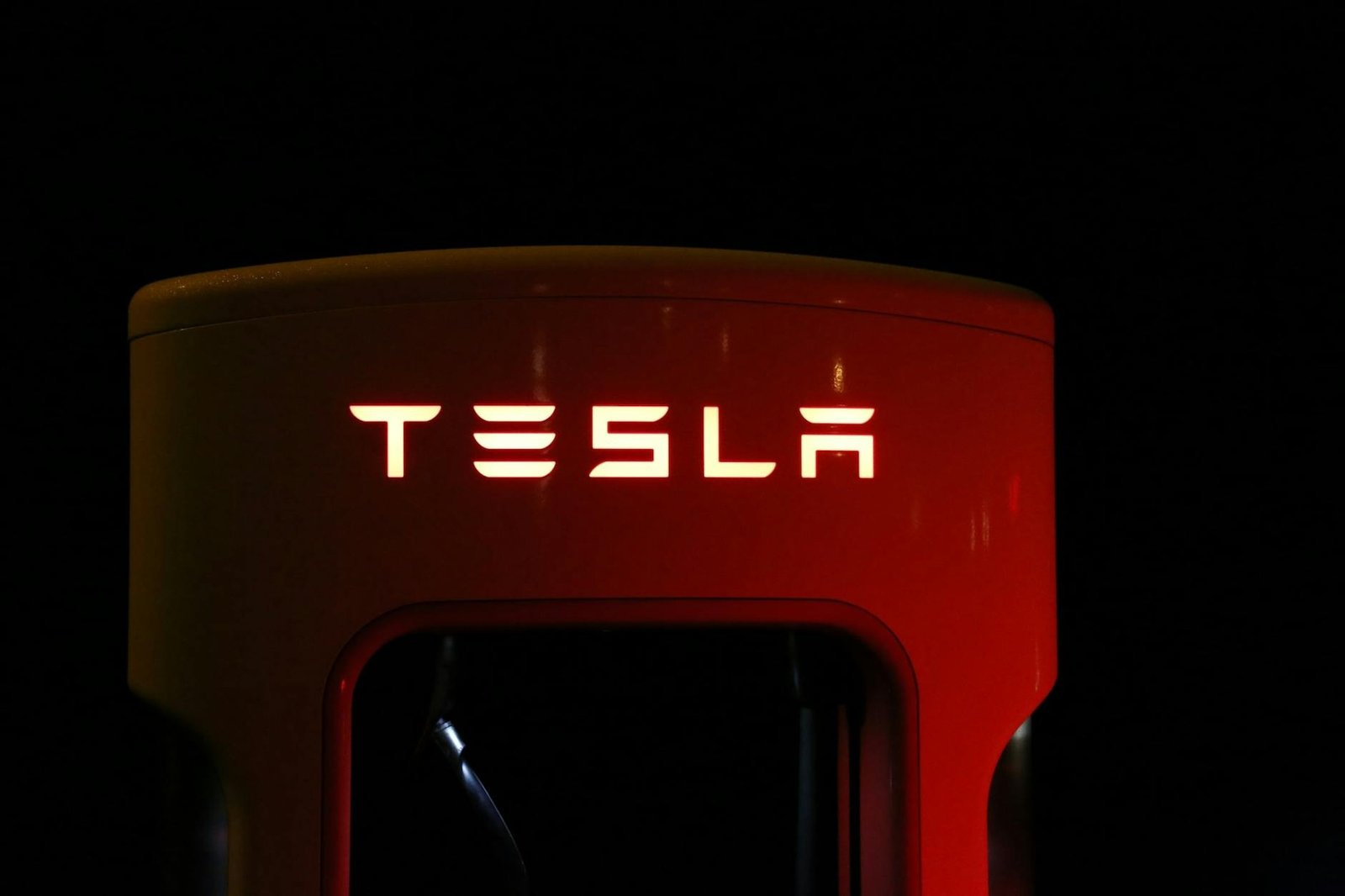 Gros plan d'une station de charge Tesla illuminée la nuit, présentant une technologie automobile moderne.