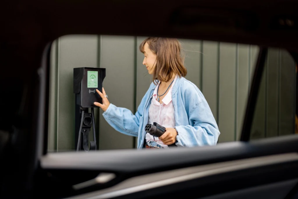 La femme allume la station de recharge de voiture tout en chargeant son véhicule électrique près de la maison.