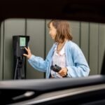 La femme allume la station de recharge de voiture tout en chargeant son véhicule électrique près de la maison.