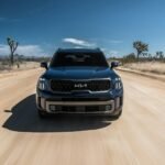 Vue avant d'un SUV conduisant rapidement sur un chemin de terre du désert sous un ciel bleu clair.