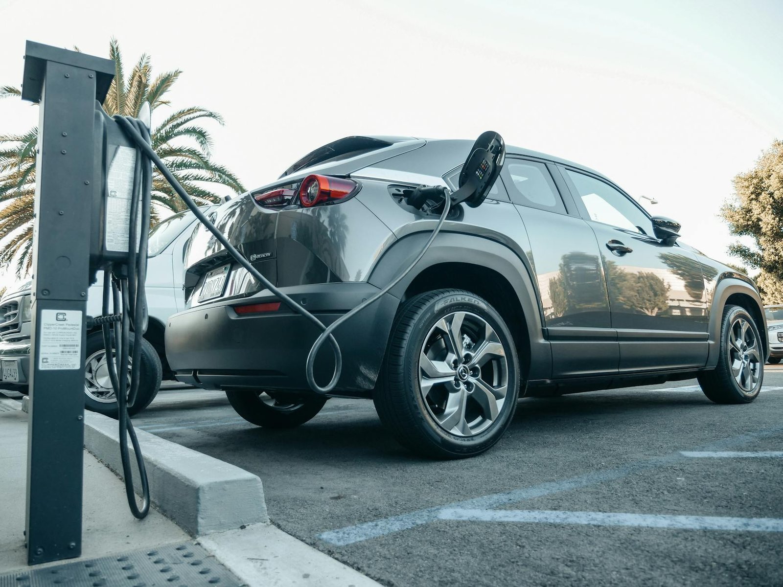 Un véhicule électrique moderne charge dans une station extérieure à la lumière du jour.