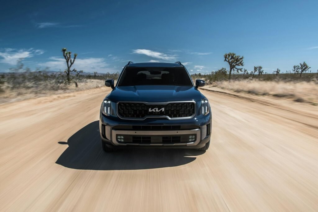 Vue avant d'un SUV conduisant rapidement sur un chemin de terre du désert sous un ciel bleu clair.