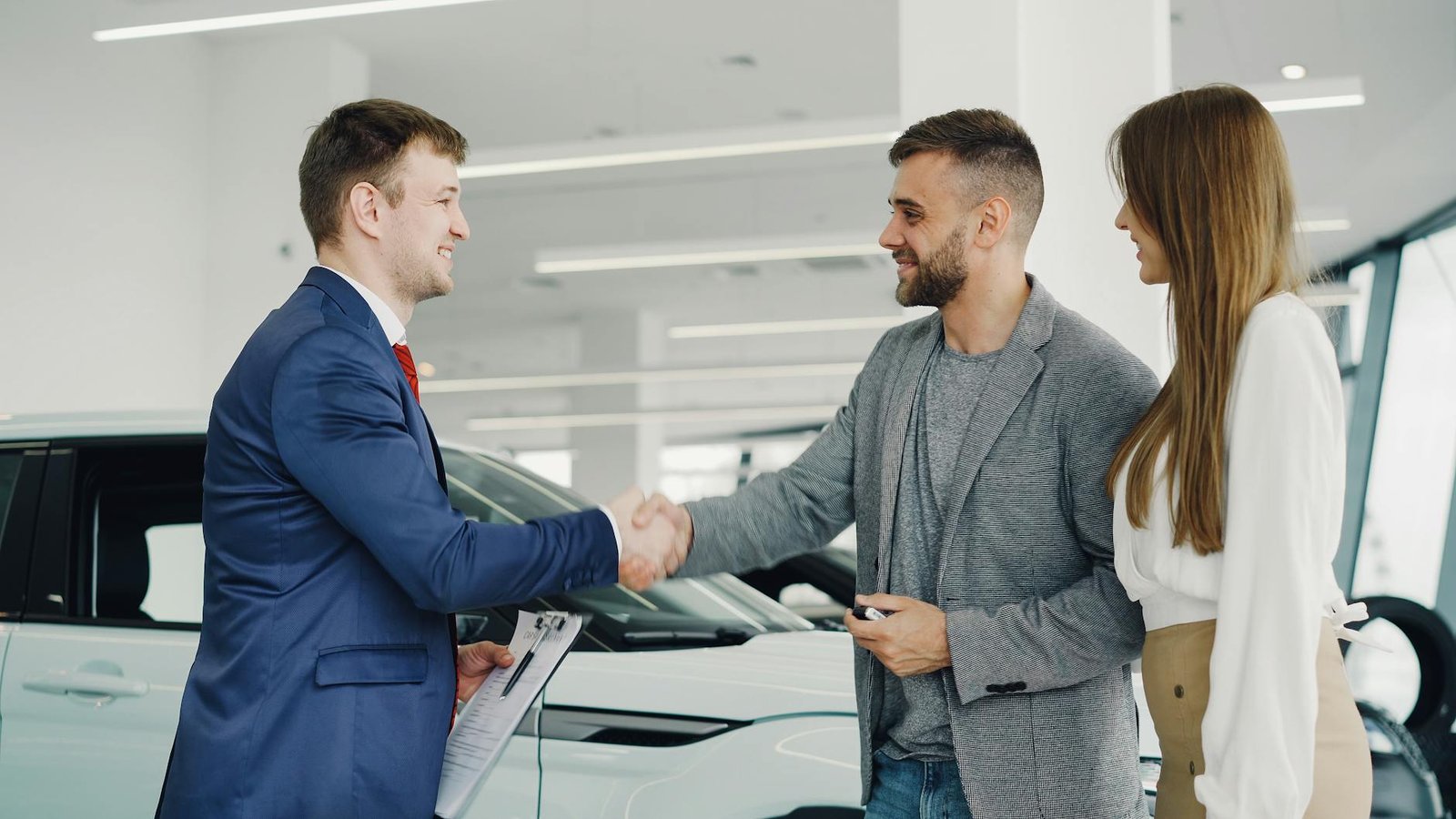 Poignée de main amicale entre un vendeur de voitures et des clients dans une salle d'exposition automobile moderne.