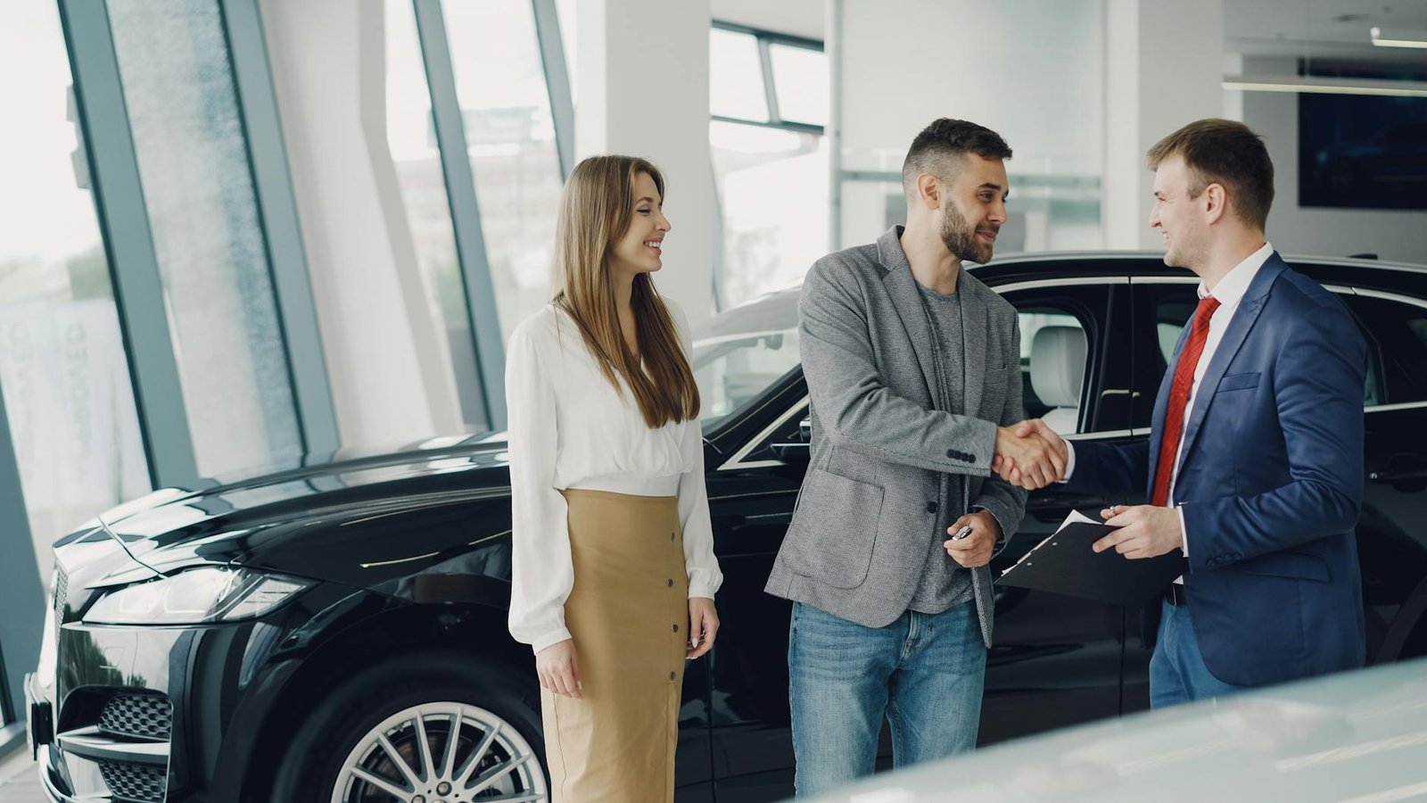 Les clients serrent la main du concessionnaire dans la salle d'exposition et concluent un accord d'achat de voiture.